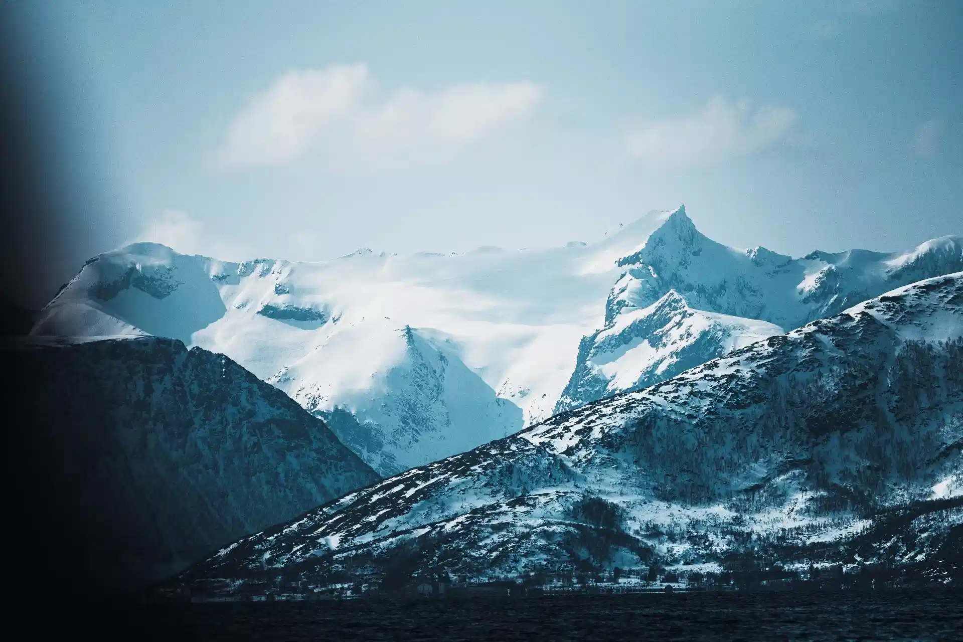 Snow-covered Arctic mountain range and glacier beneath pale clouds