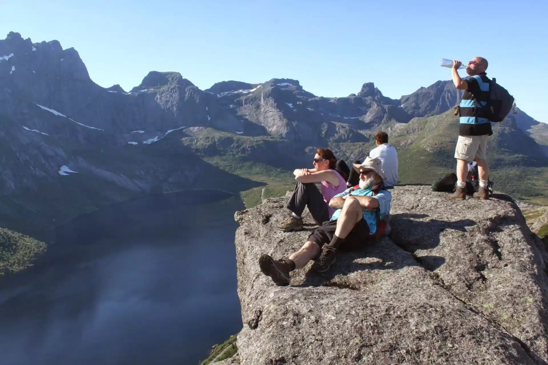 Three hikers resting on a rocky summit above a deep blue Lofoten fjord