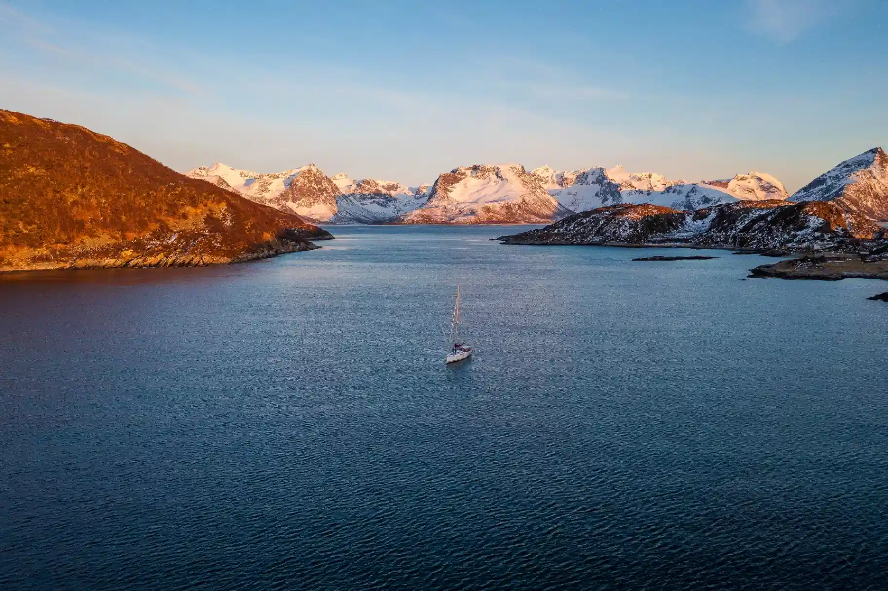 Small sailing yacht in a broad fjord beneath sunlit snow-covered mountains