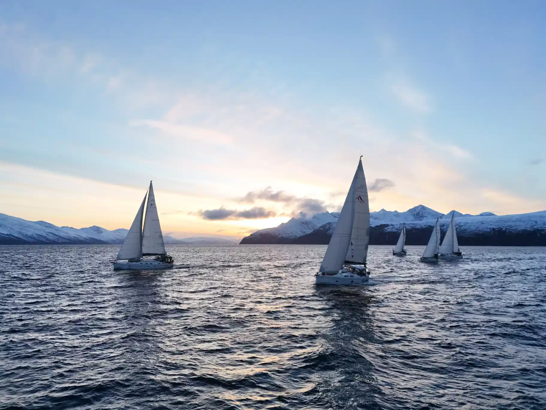 Sailing yacht under way in an Arctic Norwegian fjord below snow-covered mountains