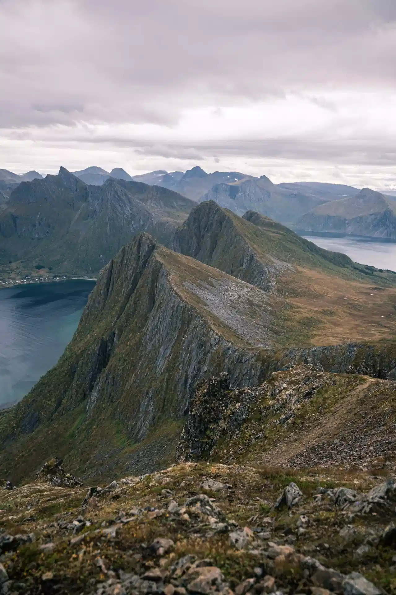 Narrow mountain ridge descending between fjords beneath an overcast sky