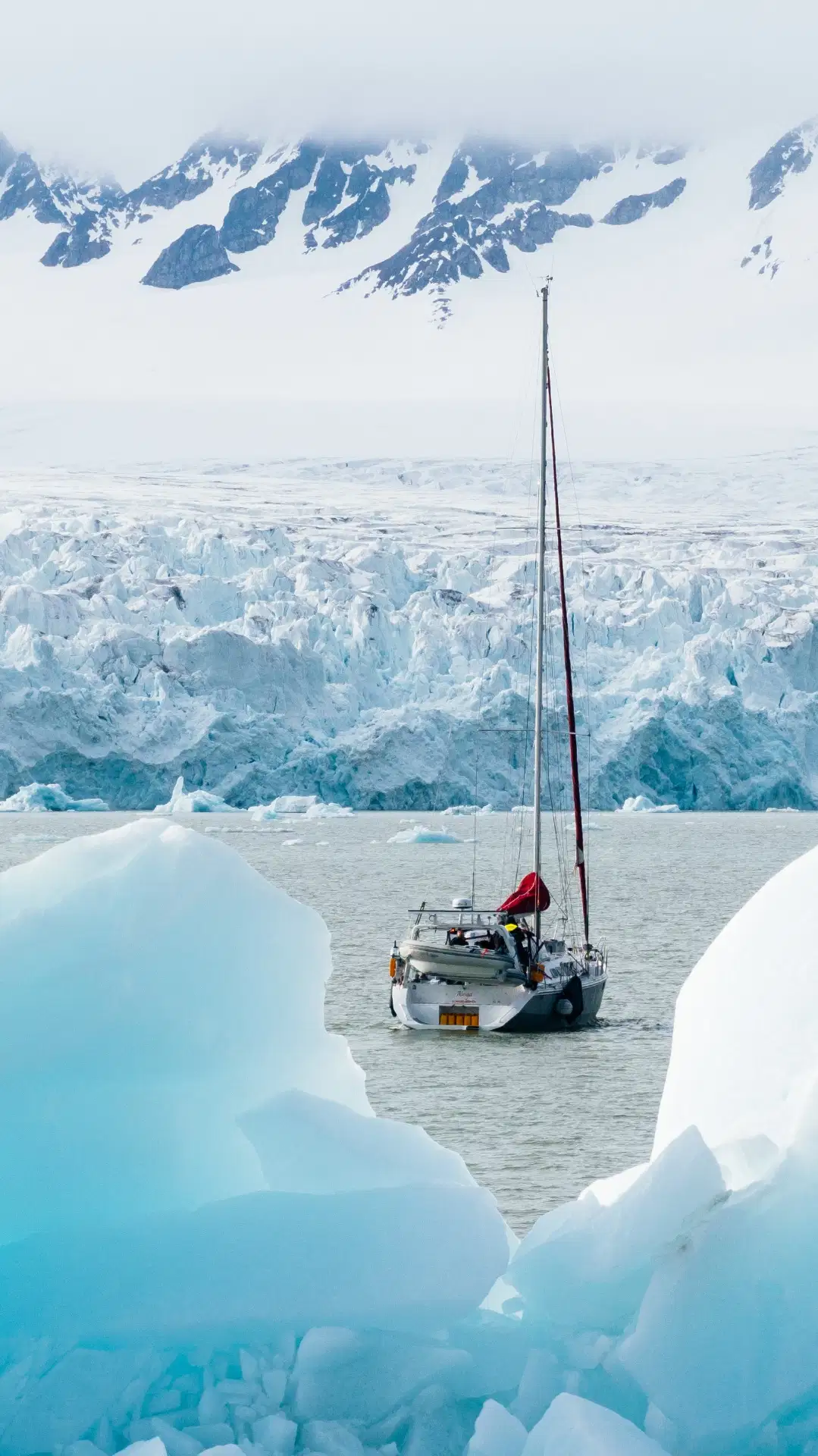 Sailing yacht among blue ice floes in front of a Svalbard glacier